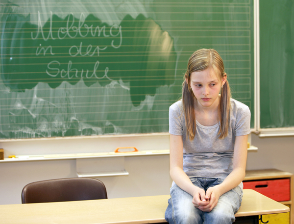 Mädchen sitzt deprimiert auf Tisch vor Schultafel